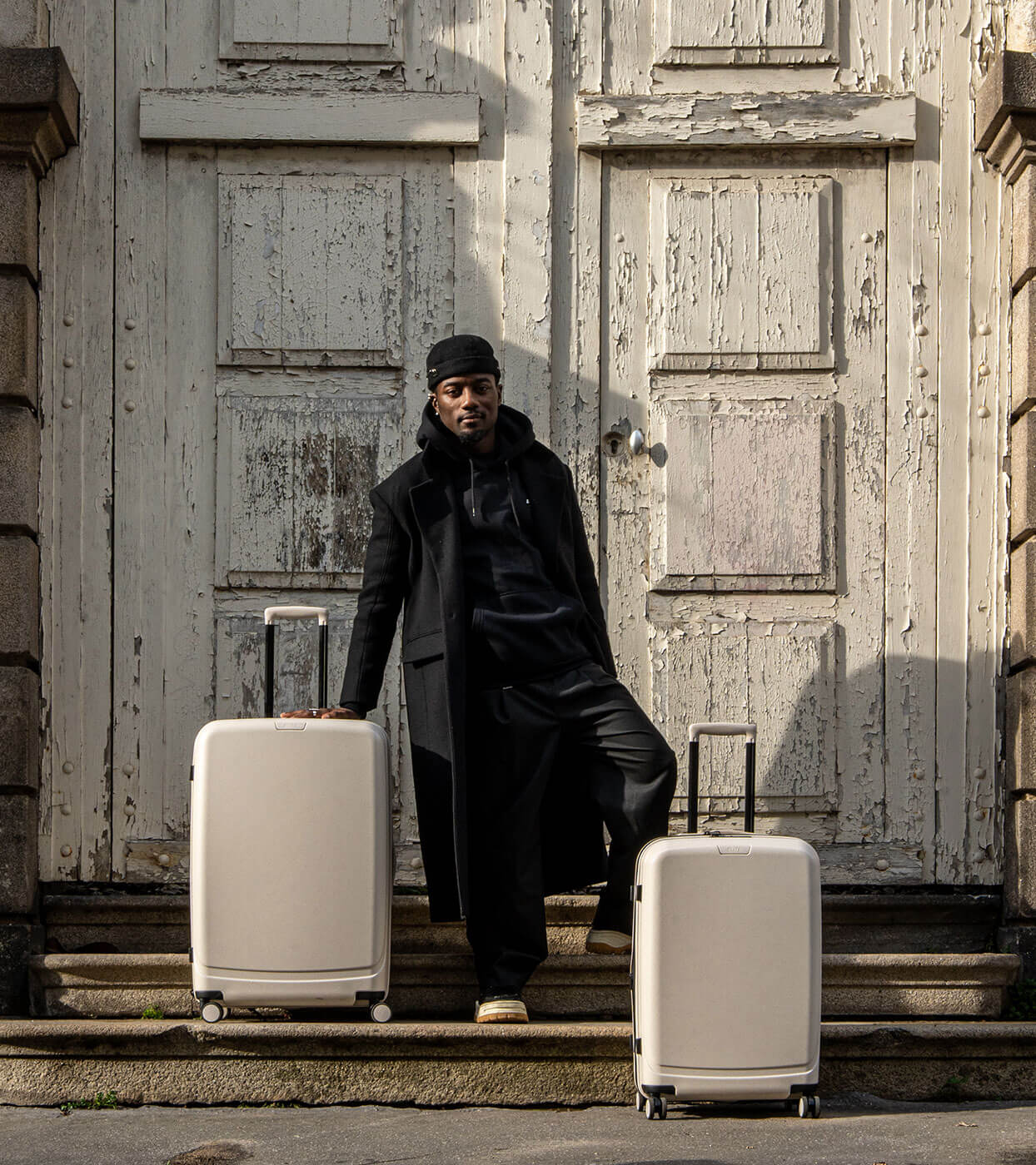 Homme habillé en noir posant la main sur des valises recyclées beiges